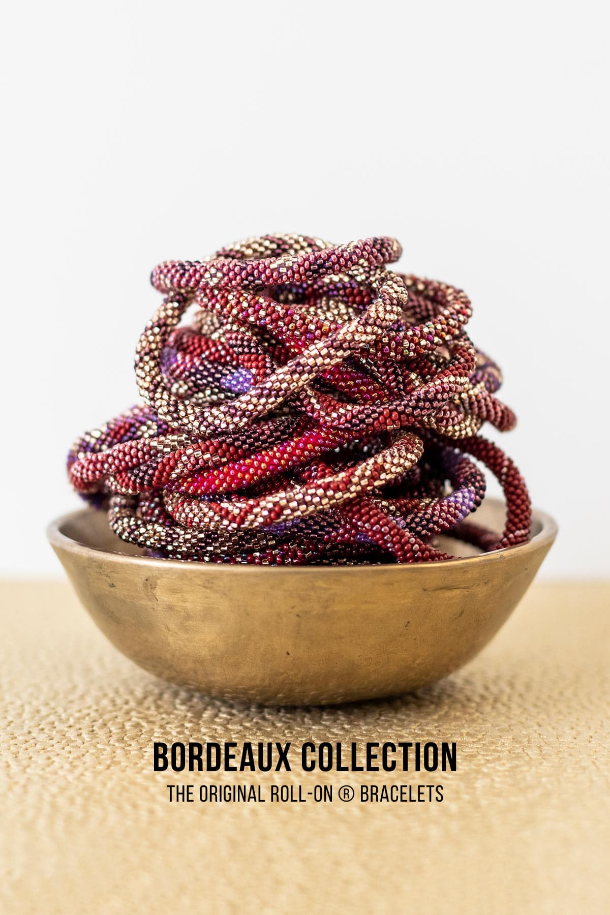 Bordeaux beaded roll-on bracelets in burgundy plum and gold piled in brass bowl — Urban Wild