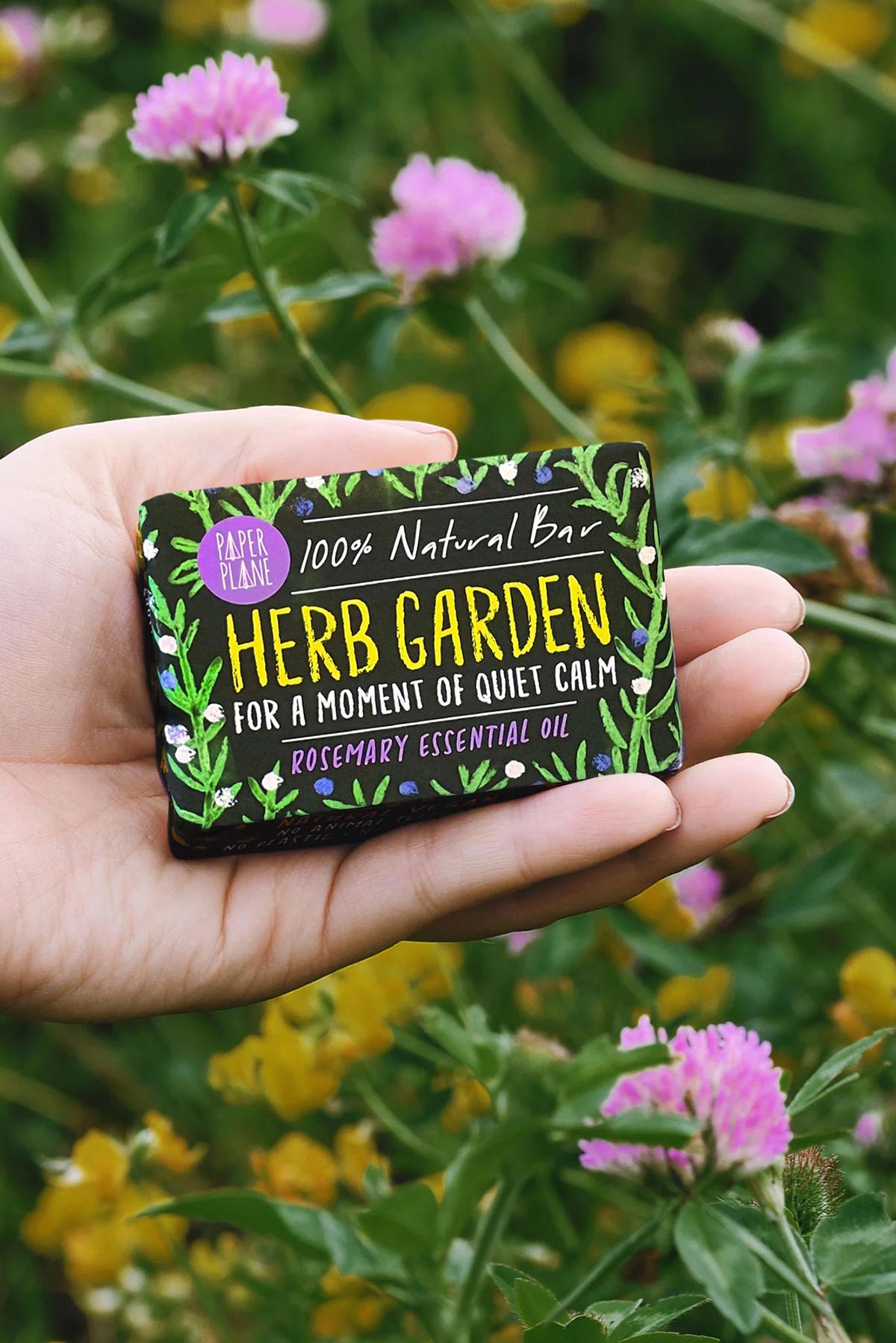 Hand holding Paper Plane Herb Garden rosemary soap bar in wildflower meadow — Urban Wild
