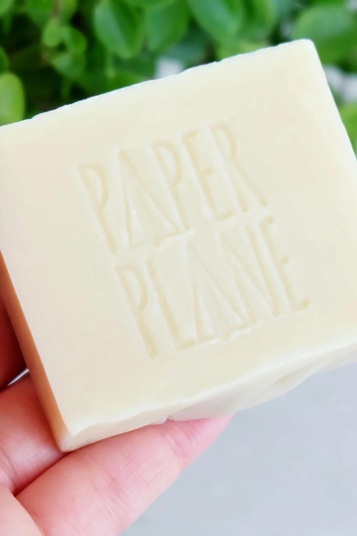 Unwrapped natural dog shampoo bar embossed with Paper Plane logo held in hand — Urban Wild